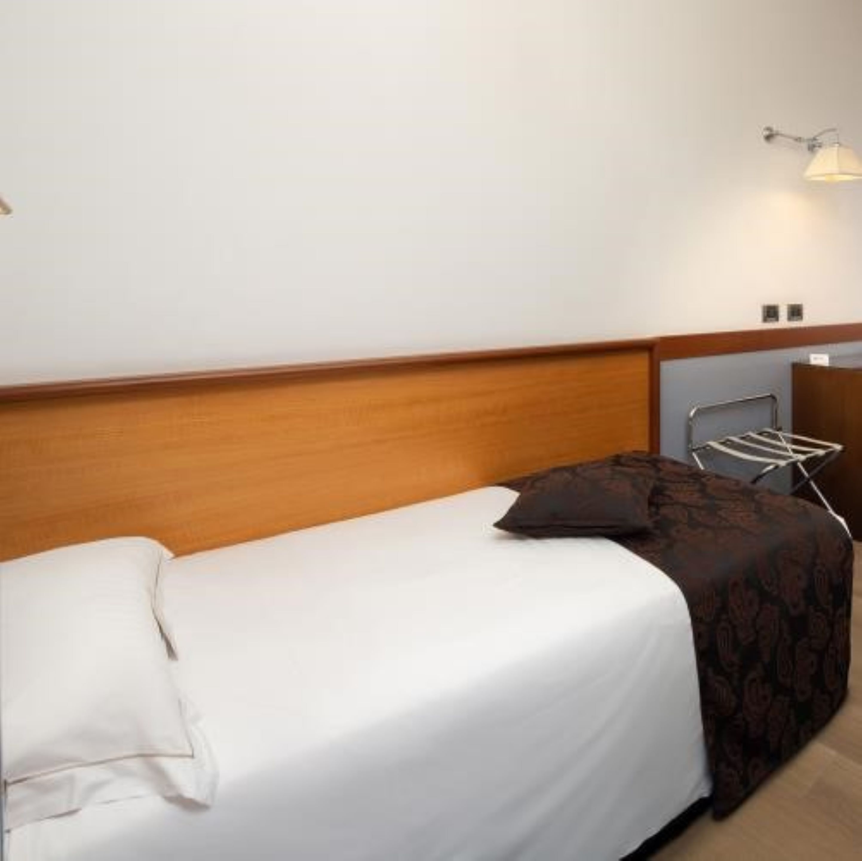 Una cama individual con cabecera de madera, colchón blanco y manta oscura estampada.