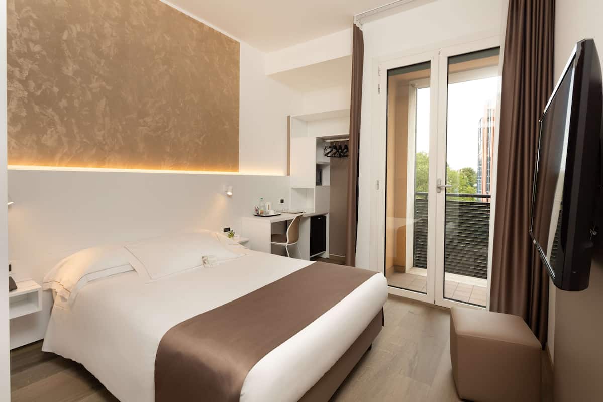 Une chambre d’hôtel moderne dotée d’un grand lit, d’un bureau, d’une chaise, d’une télévision et d’un balcon avec des rideaux.