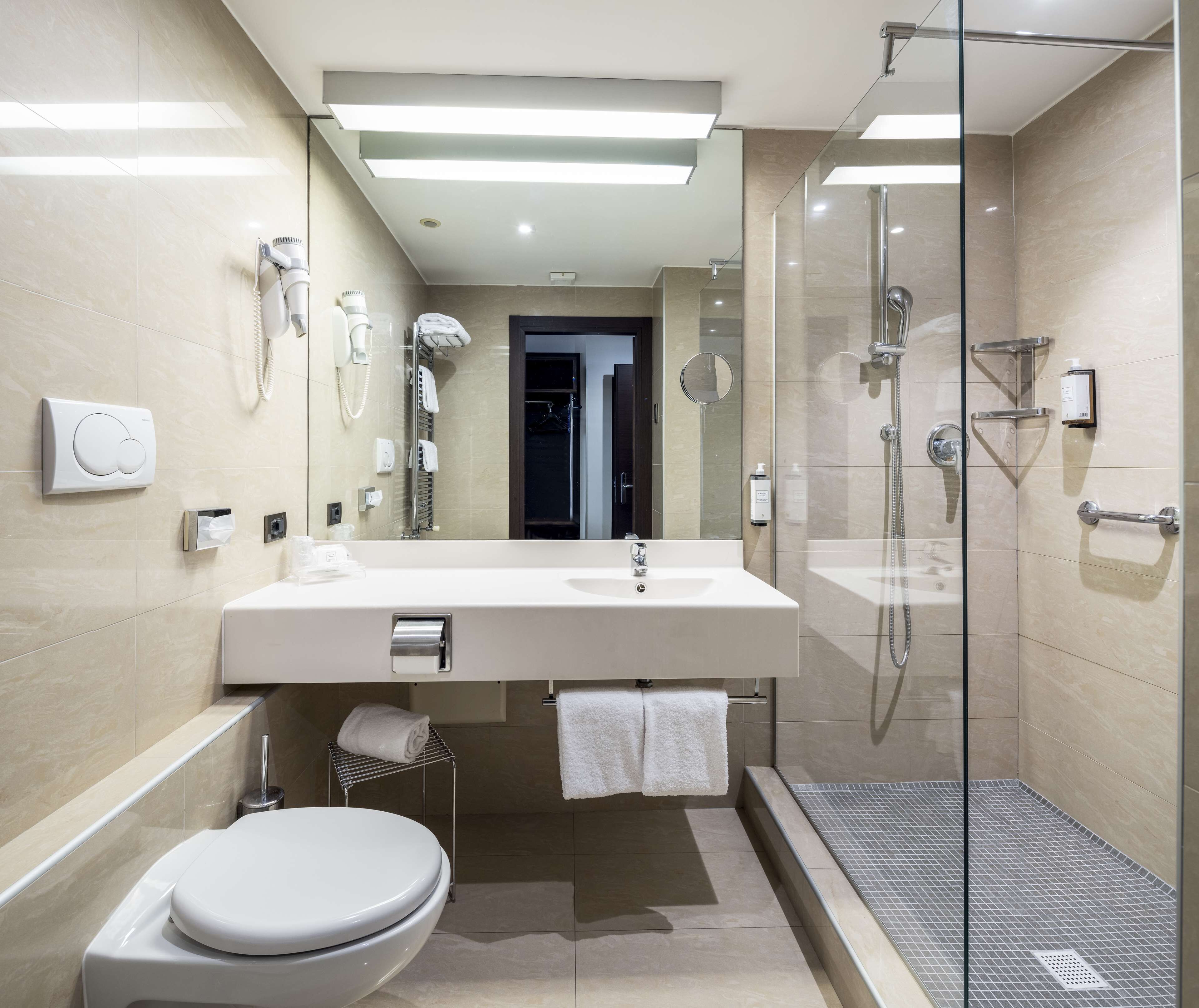 Un baño moderno con ducha de vidrio, lavamanos blanco y retrete.