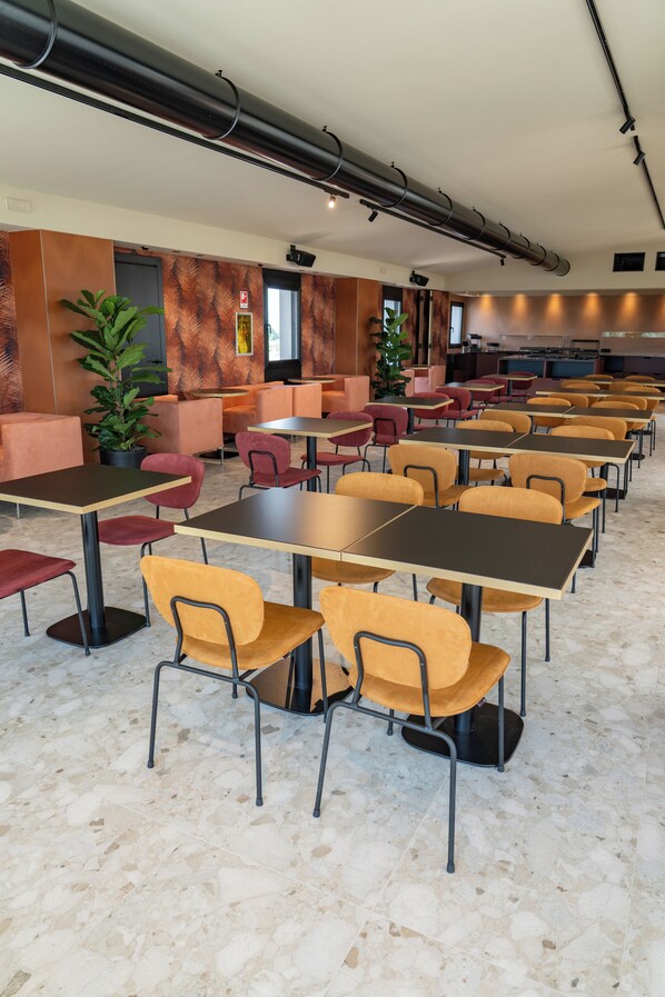 A modern dining area with multiple tables and chairs, a large potted plant, and a kitchen in the background. - Best Western Hotel Biri (Padova)