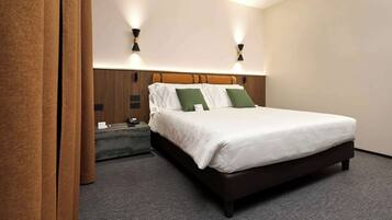 A neatly made bed with white bedding and green pillows, a wooden headboard, and two wall-mounted light fixtures.