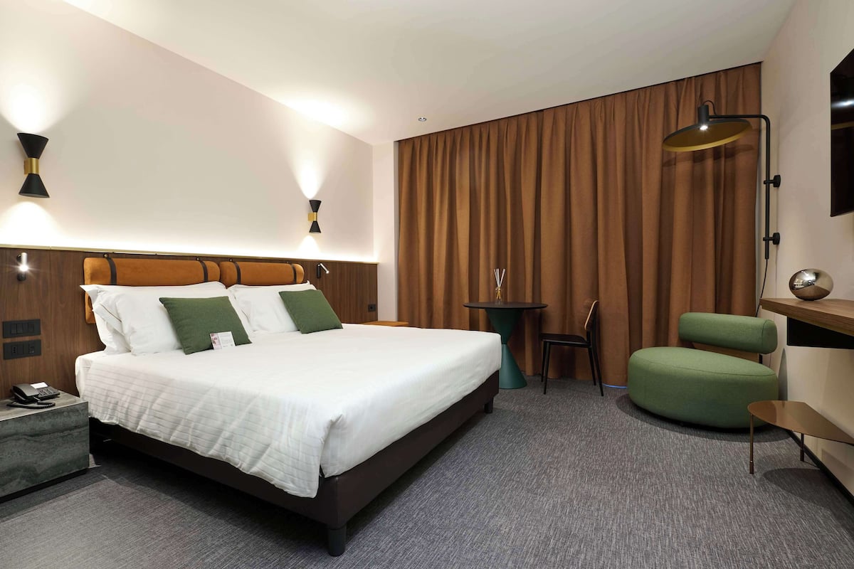 Une chambre d’hôtel avec un grand lit, un bureau avec un téléphone, une chaise verte, une petite table et une lampe.
