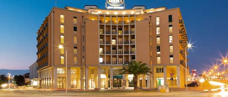 A multi-story hotel with a prominent sign at the top, a well-lit entrance, and a parking area in front.