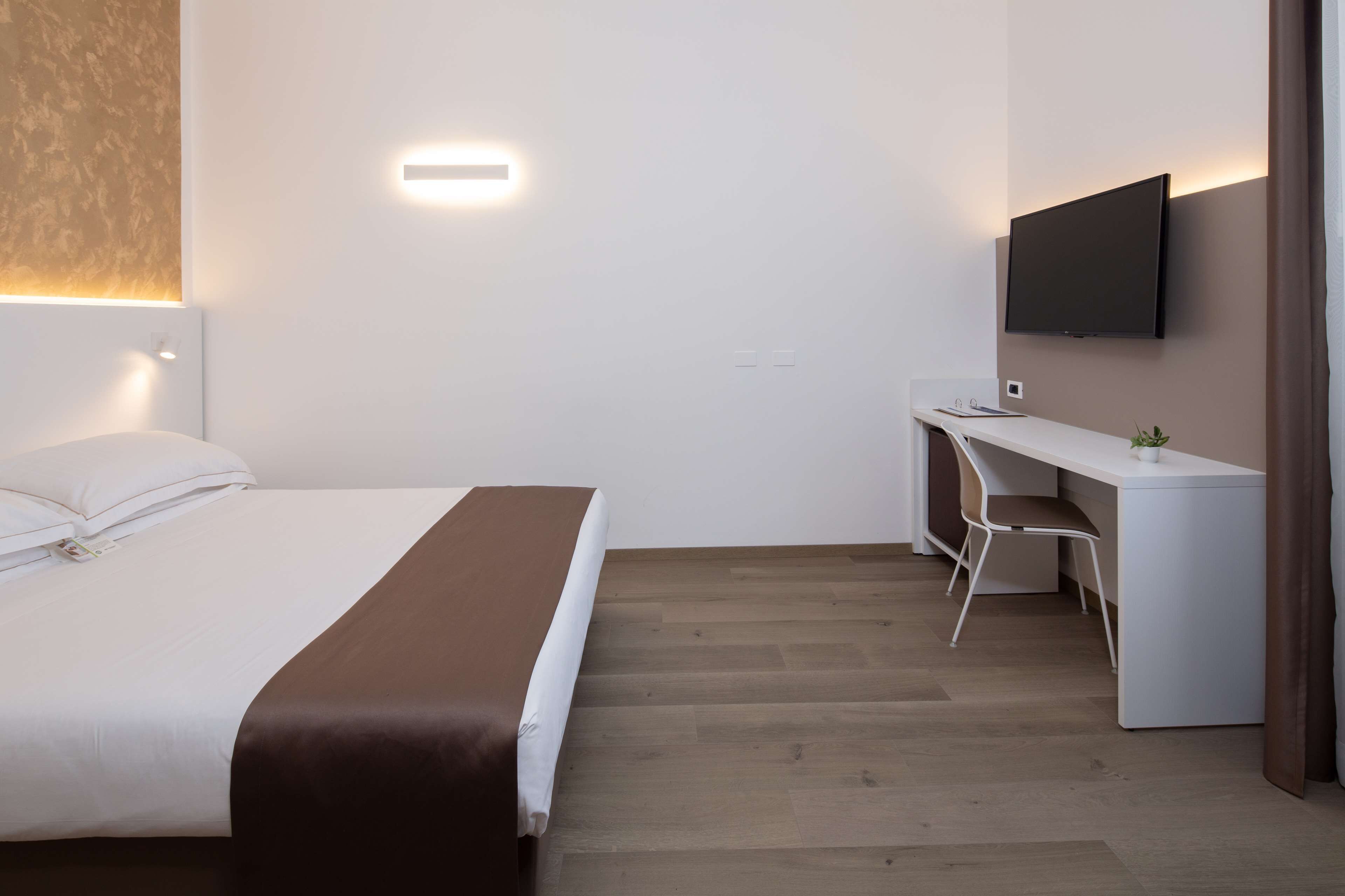 Een hotelkamer met een bed, een bureau, een stoel, een flatscreen-tv en een wandlamp.
