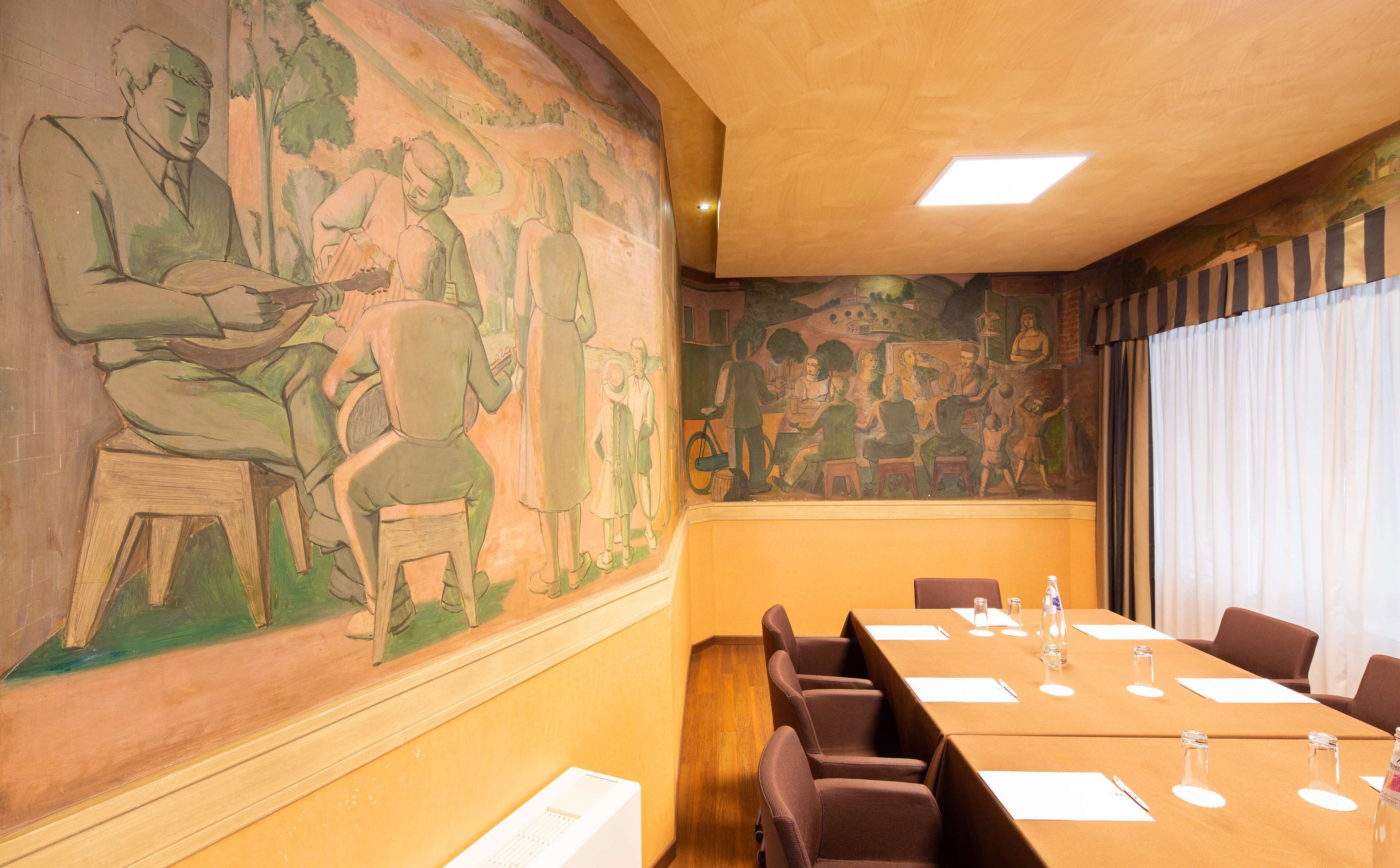 A conference room with a mural on the wall, a long table with chairs, and a window with curtains.
