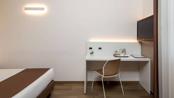 Quarto de hotel com cama, escrivaninha com cadeira, televisão de tela plana e luminária na parede.