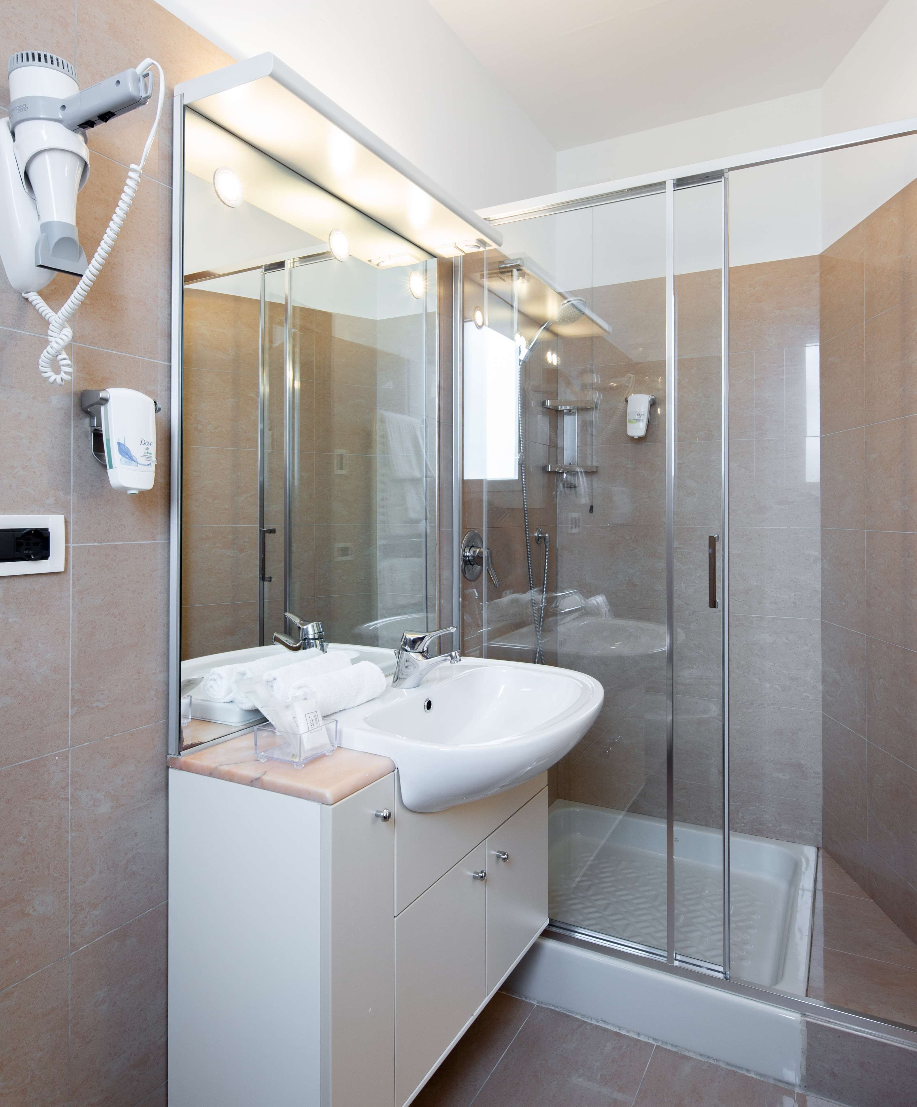 A modern bathroom with a glass shower enclosure, a double sink vanity, and a hairdryer mounted on the wall.