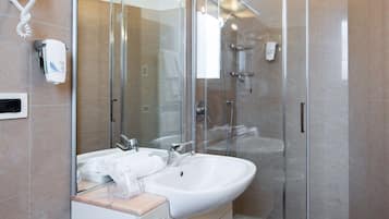 A modern bathroom with a glass shower enclosure, a double sink vanity, and a hairdryer mounted on the wall.