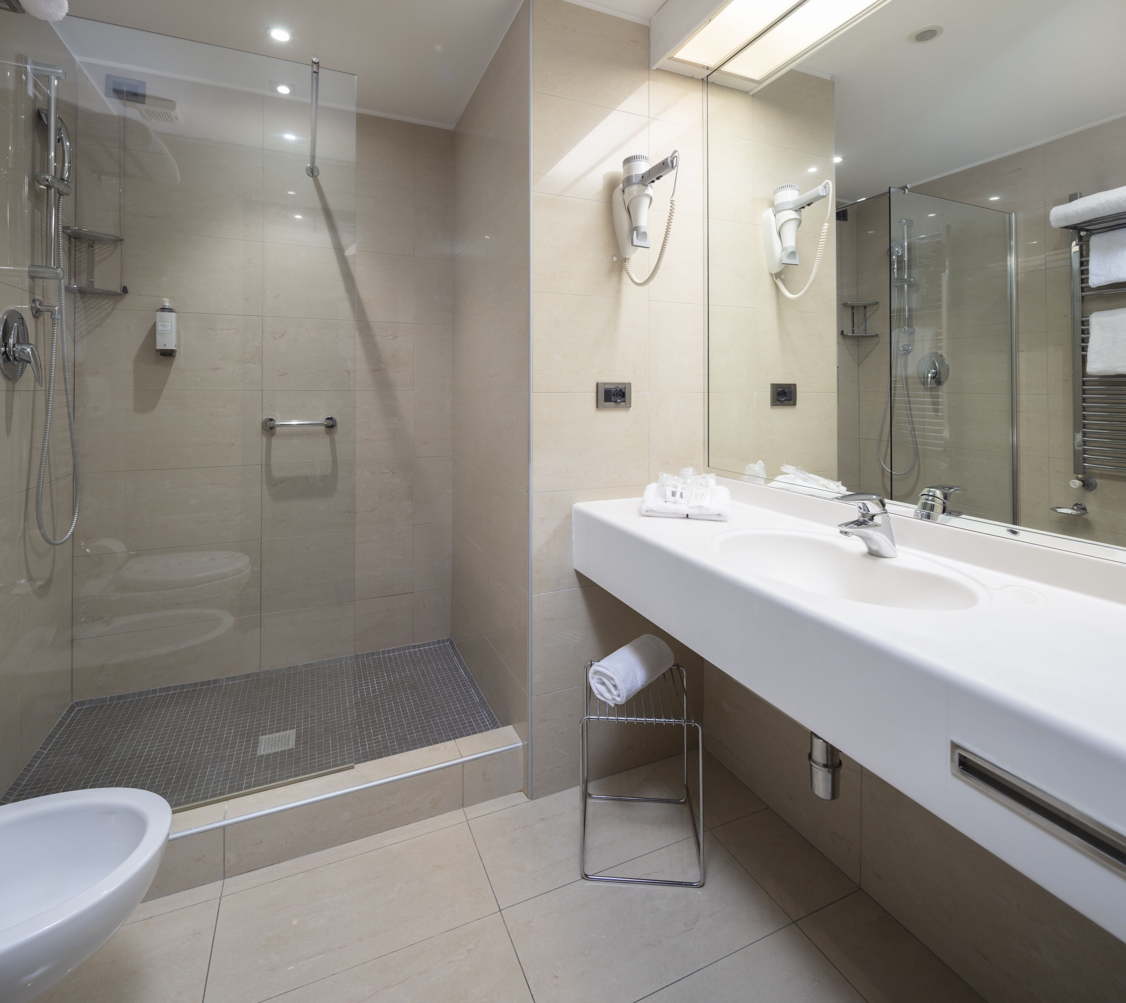 A modern bathroom with a glass-enclosed shower, a large mirror, and a white sink.