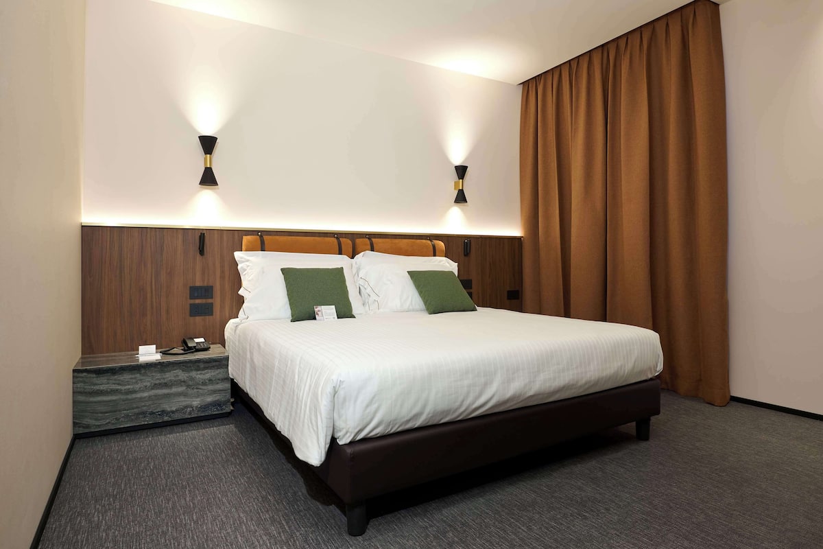 Une chambre d’hôtel avec un grand lit, deux tables de chevet, une tête de lit en bois et deux lampes fixées au mur.