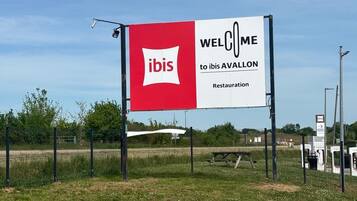 A large billboard with the ibis logo and the text 'WELCOME to ibis AVALLON' indicating a restaurant.
