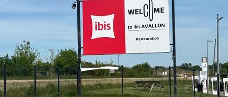 Un cartel grande con el logo de ibis y el texto 'WELCOME to ibis AVALLON' que indica un restaurante.