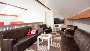 Een kamer met hoge plafonds, een plafondventilator, een wandgemonteerde flatscreen-tv en een schaakbord op een bijzettafeltje.