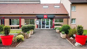 Een hotel met een rood pannendak, een glazen ingang en rode plantenbakken aan de voorzijde.