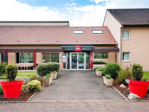 A hotel with a red tiled roof, a glass entrance, and red planters in the front. - Hotel ibis Avallon (Magny)
