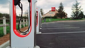 Een Tesla laadstation met een helder uitzicht op de omgeving, waaronder een weg, een restaurant en een hotel genaamd "ibis".