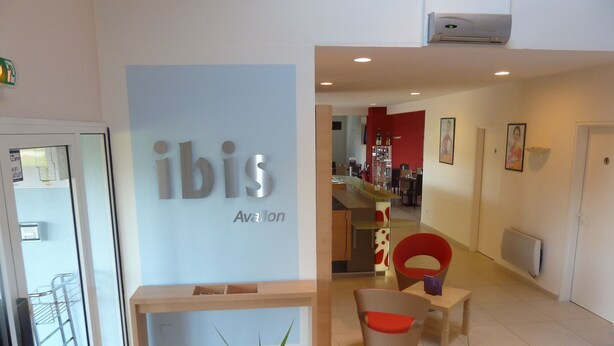 Een receptiegedeelte met een bord waarop 'ibis Avalon' staat, een houten bank en plantenbakken.