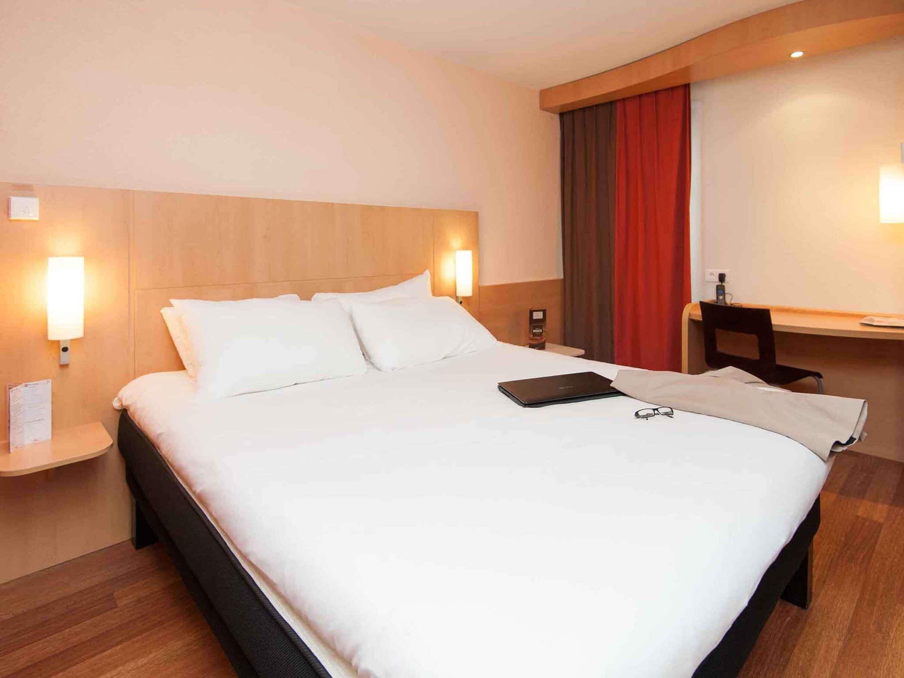 A hotel room with a bed, bedside tables, a desk, and a chair.