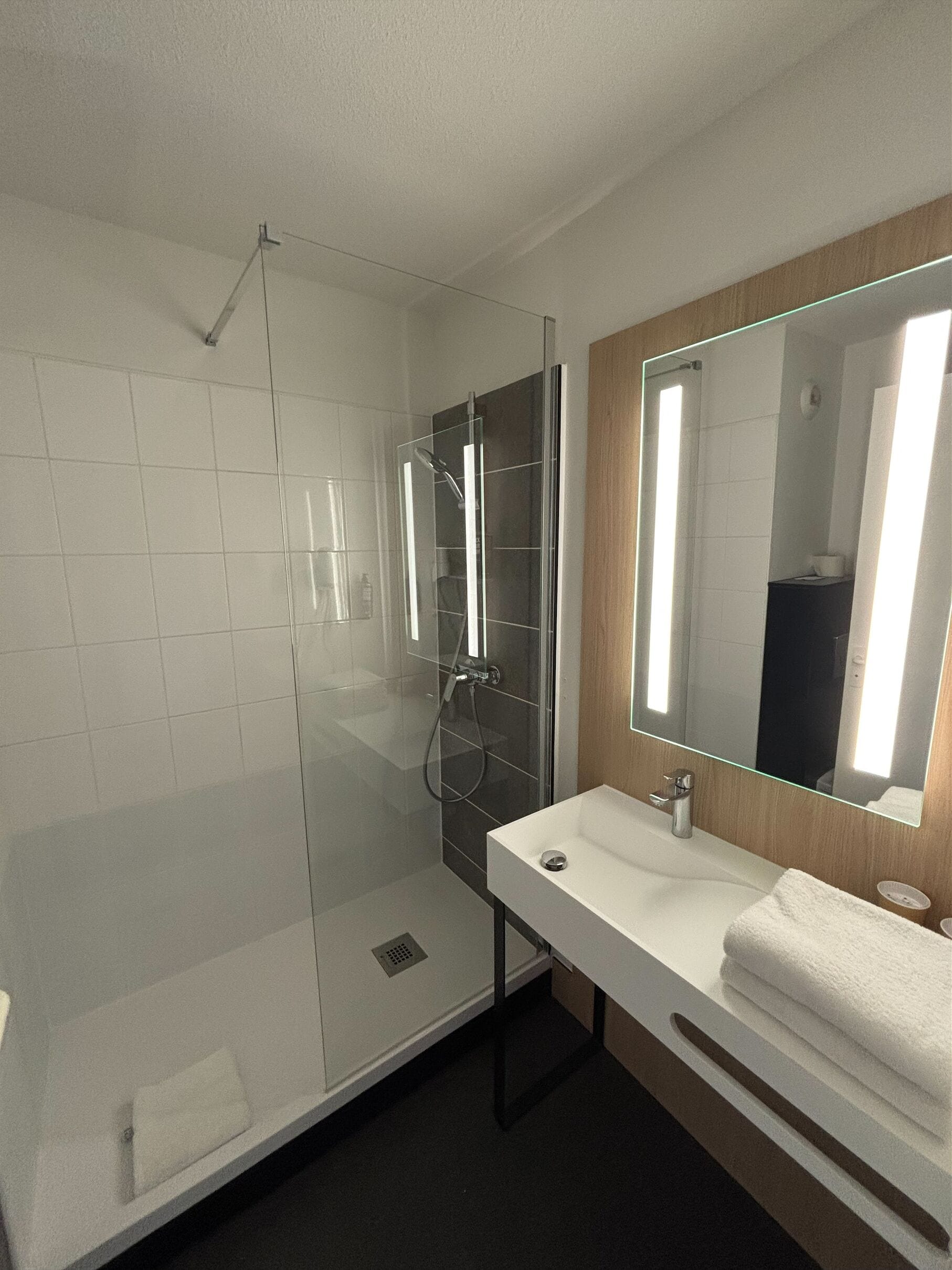 A modern bathroom with a glass-enclosed shower, a white sink, a large mirror, and a wooden vanity.