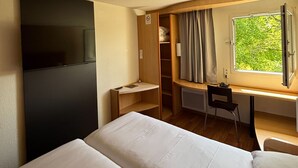 Een hotelkamer met een bed, een bureau, een stoel, een televisie en een raam met gordijnen.