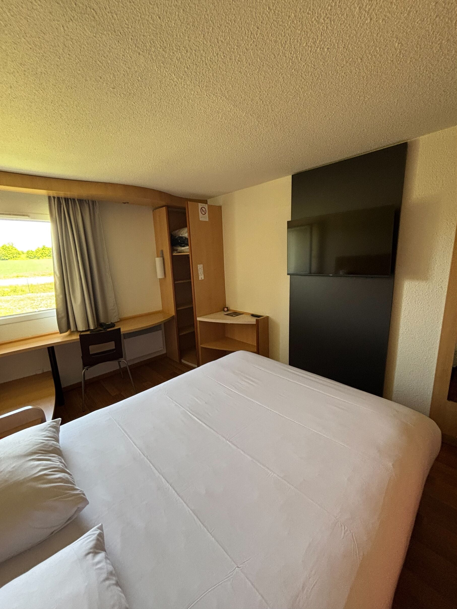 A hotel room with a bed, a desk, a chair, a TV, and a wardrobe.