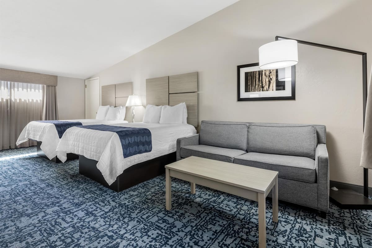 A hotel room with a bed, a sofa, a table, and a lamp.