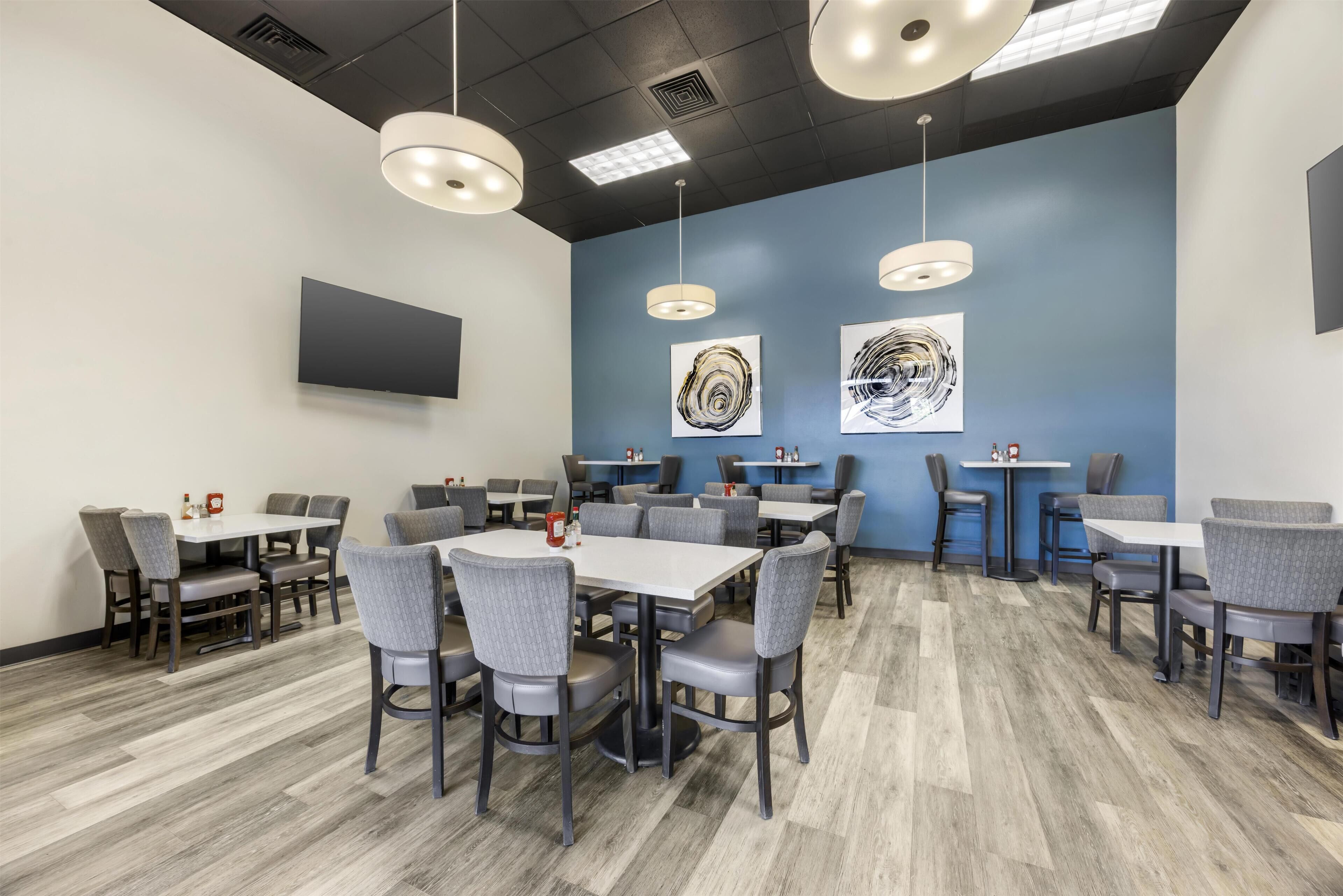 A modern restaurant with multiple tables and chairs, ceiling lights, and abstract wall art.