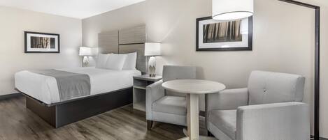 A hotel room with a bed, a desk, a chair, a round table, and two lamps.