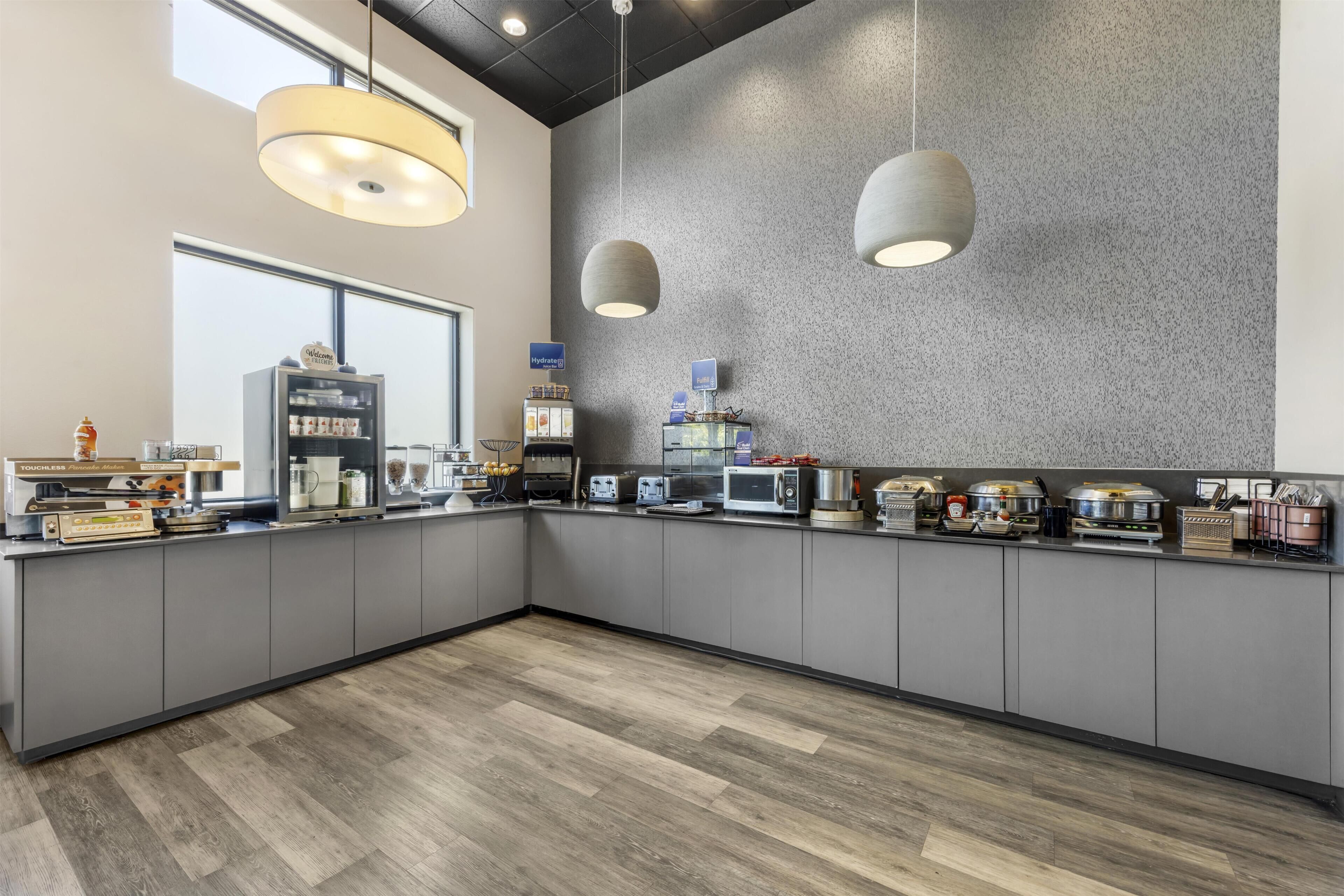 A modern kitchen with grey cabinets, a wood floor, and pendant lighting.