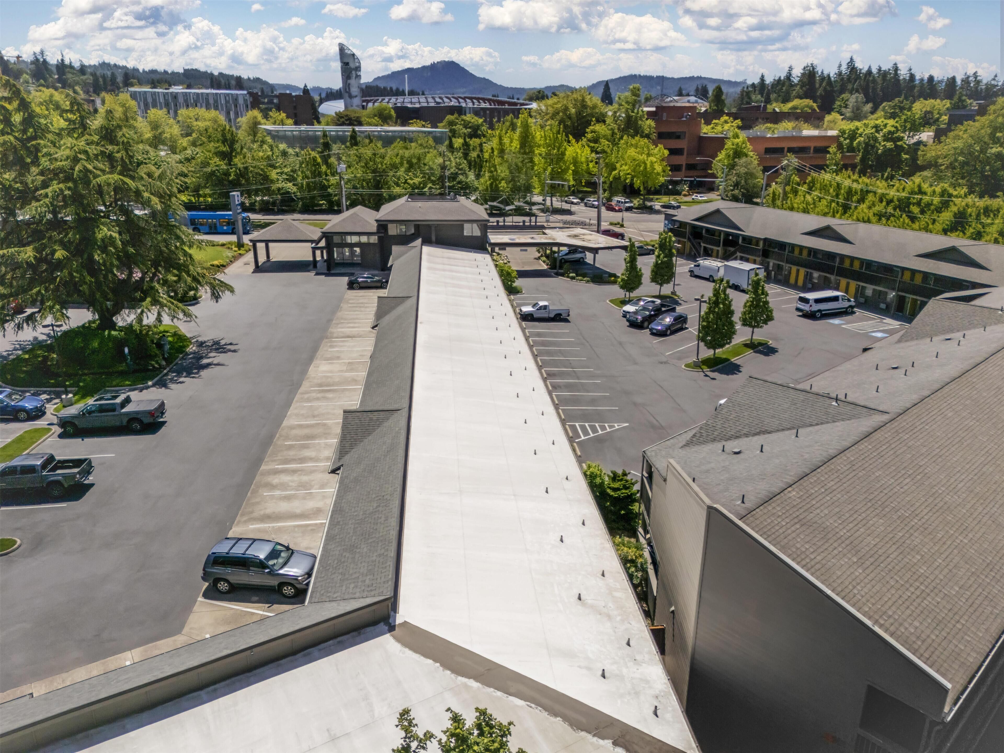 An aerial view of a parking lot with multiple cars, a building with a flat roof, and a mountain in the background.
