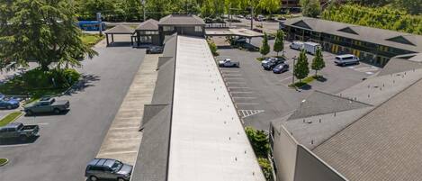 An aerial view of a parking lot with multiple cars, a building with a flat roof, and a mountain in the background.