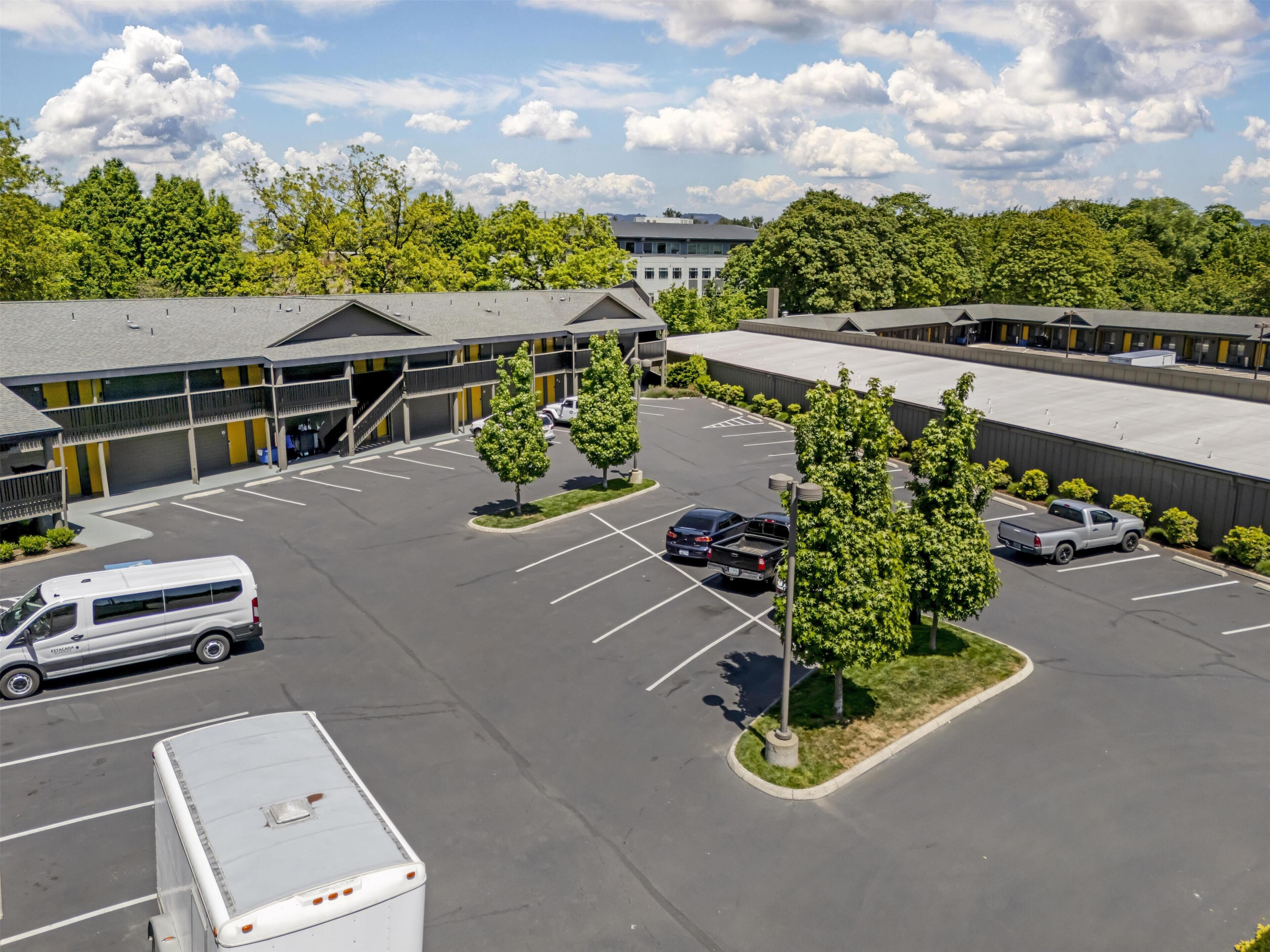 A parking lot with several vehicles, a building with a flat roof, and trees.