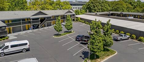 A parking lot with several vehicles, a building with a flat roof, and trees.