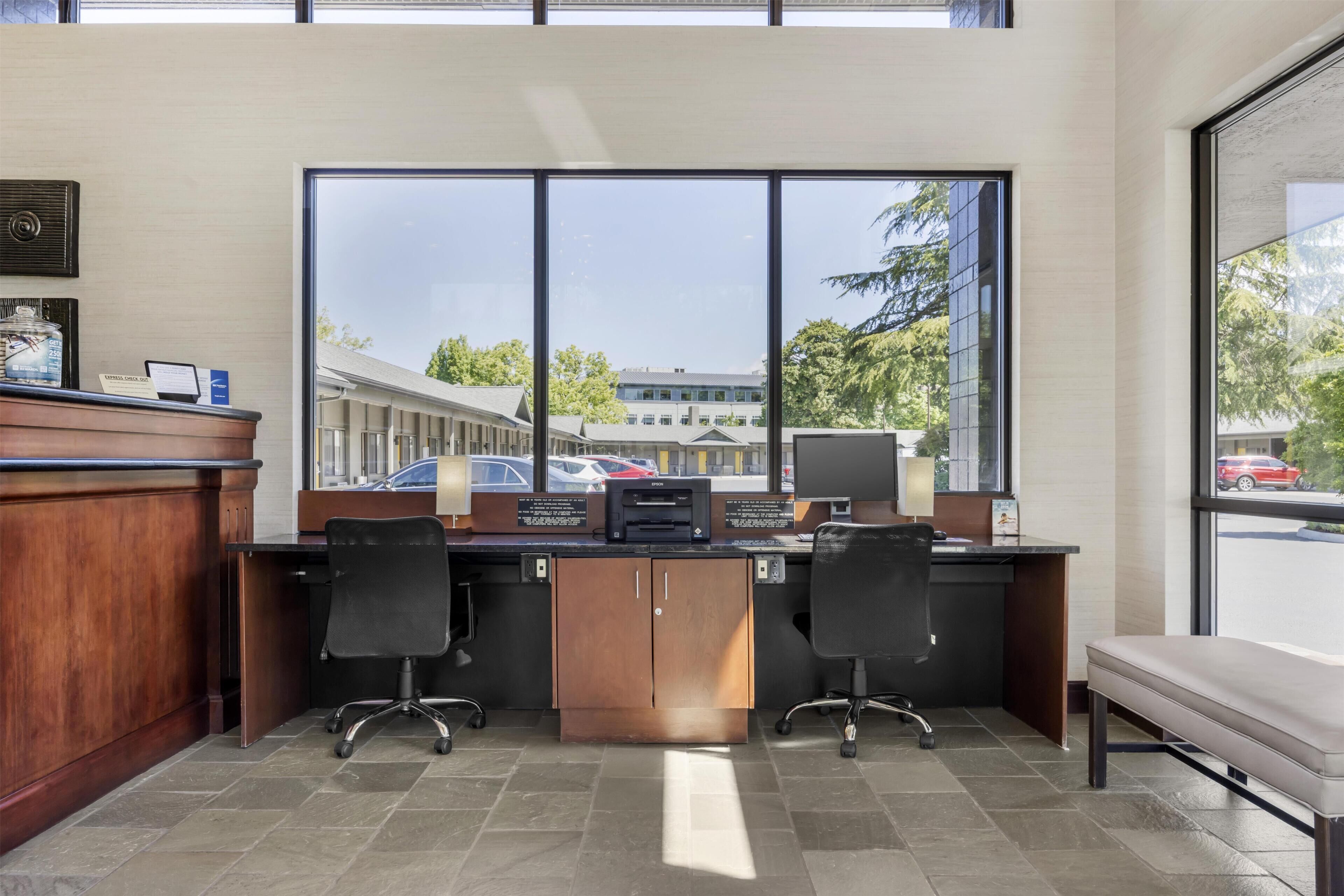 A reception desk with two chairs, a bench, and large windows offering a view of a building and parked cars.
