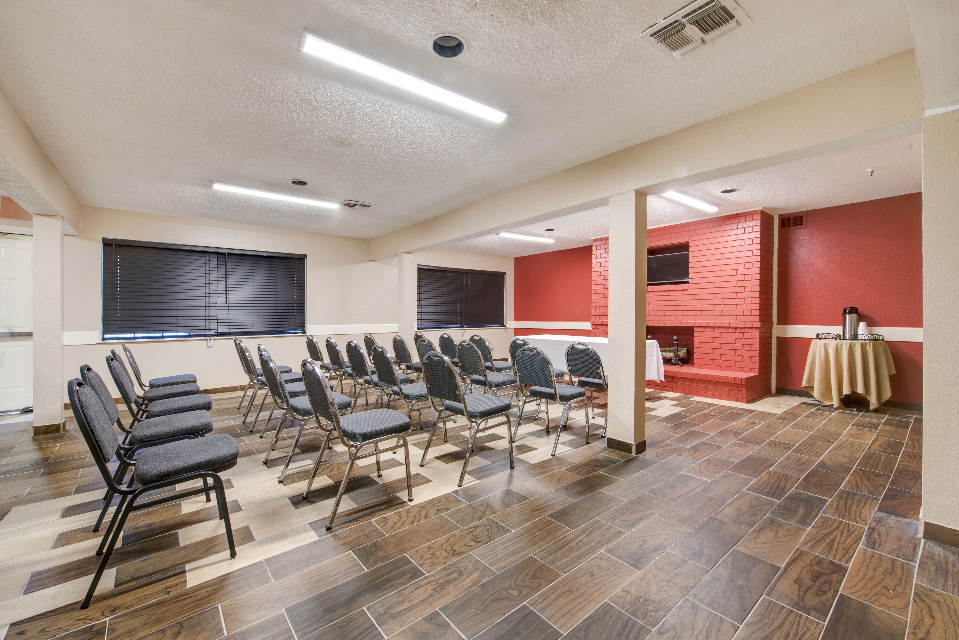 A conference room with rows of chairs, a red brick wall, and a tiled floor.
