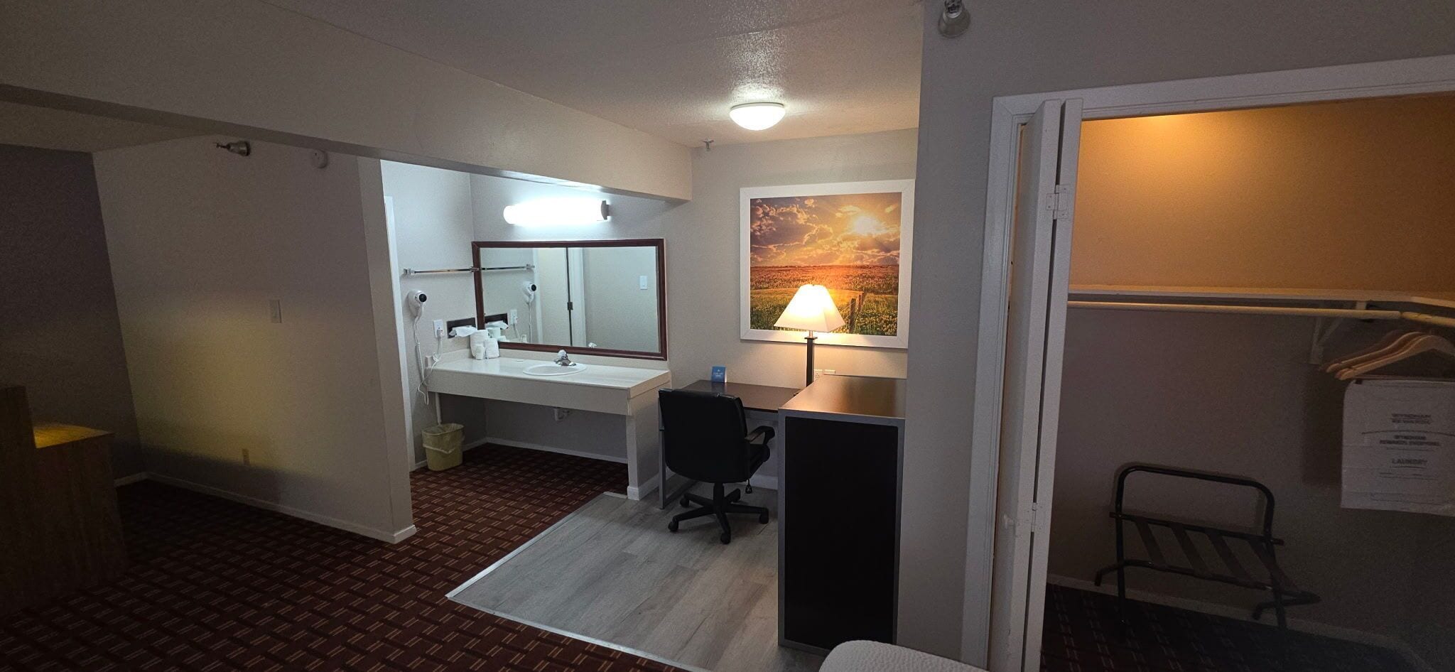 Una habitación de hotel con baño, escritorio, silla, lámpara y un cuadro en la pared.