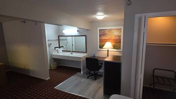 Una habitación de hotel con baño, escritorio, silla, lámpara y un cuadro en la pared.