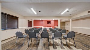 A conference room with rows of chairs, a red accent wall, and a tiled floor. - Howdy Hotel (College Station)