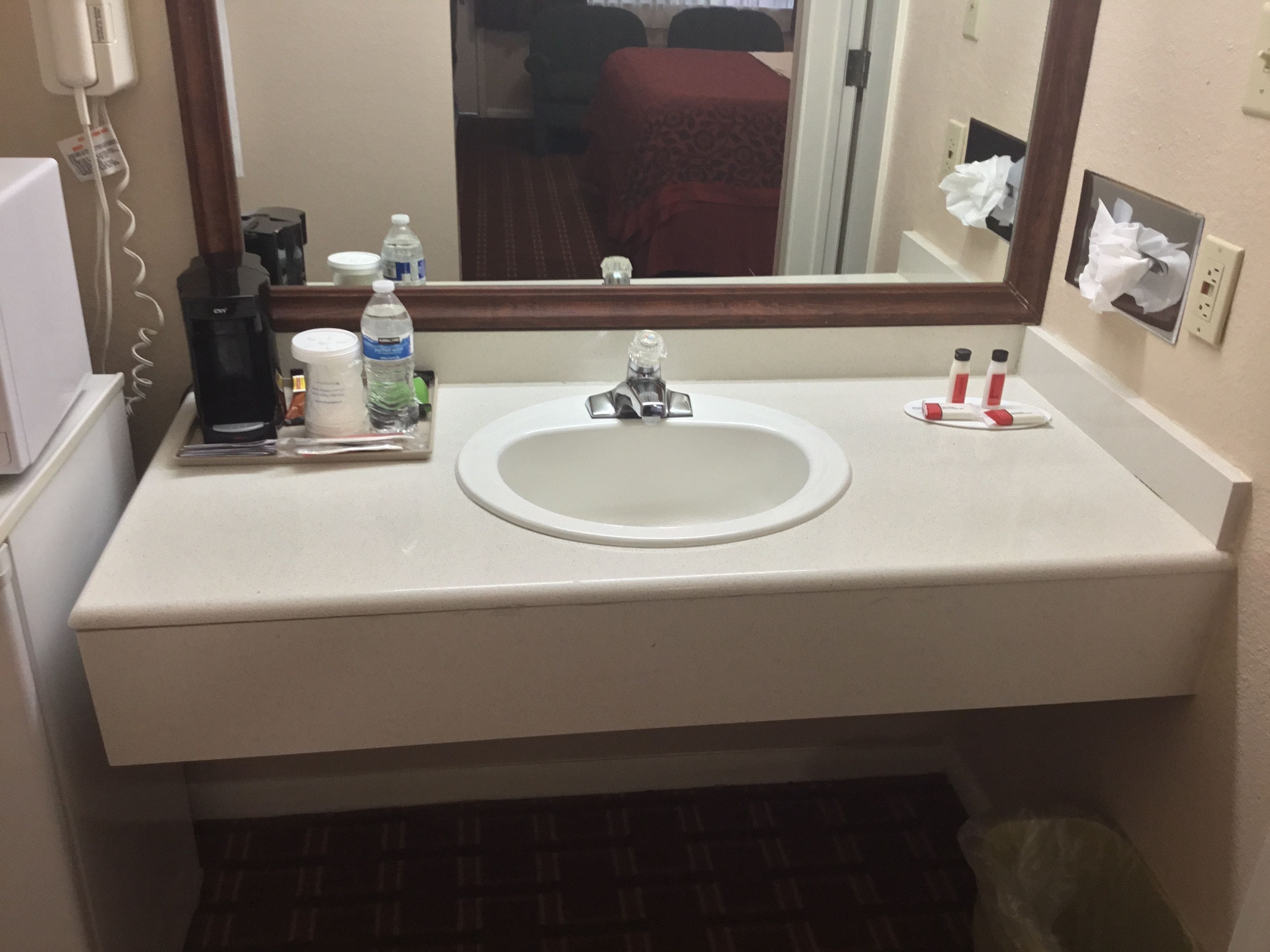 A hotel bathroom with a sink, mirror, and toiletries.