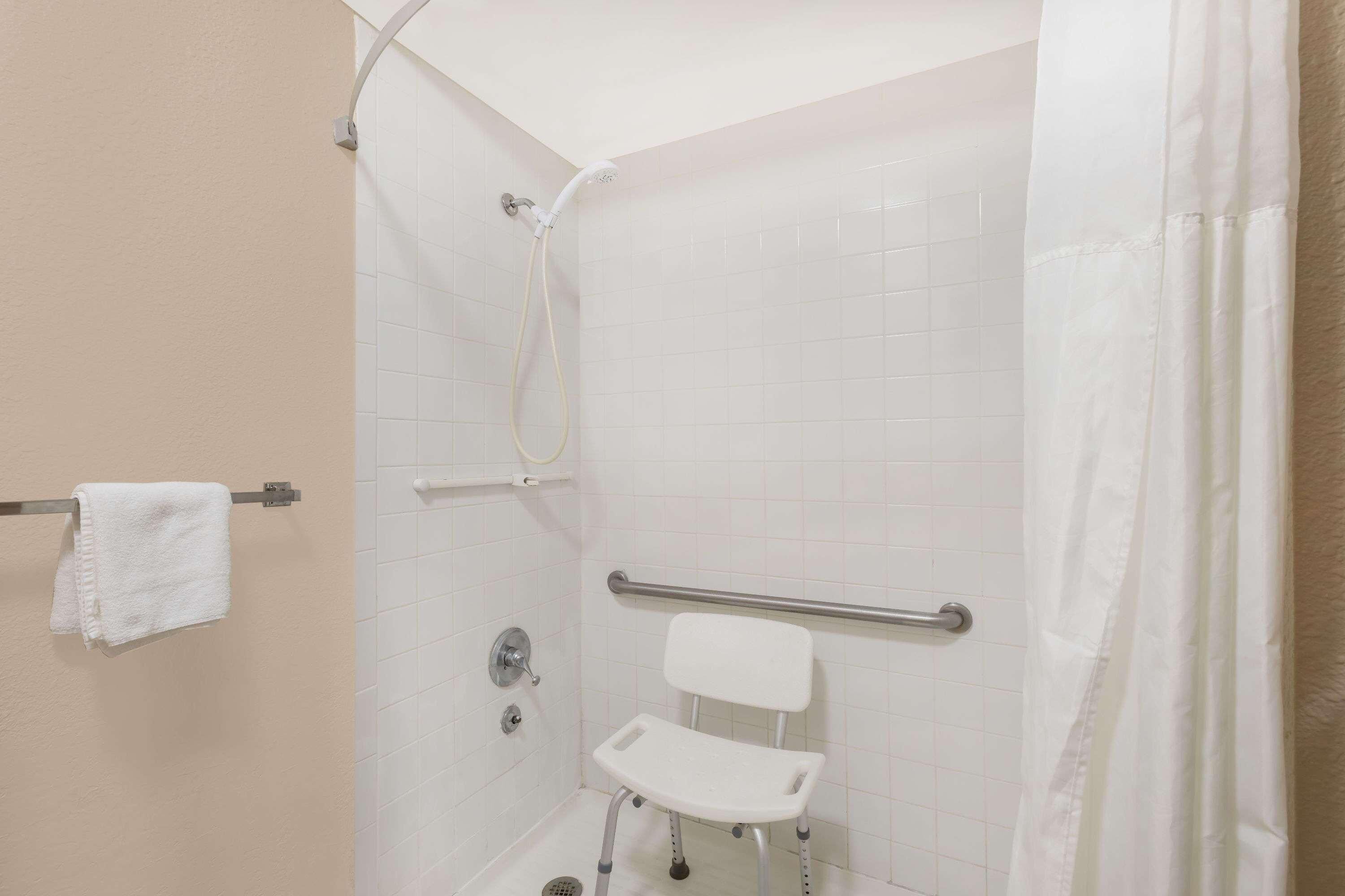 Eine Dusche mit Haltegriff, ein weißer Stuhl und ein Handtuchhalter.