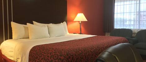 A hotel room with a large bed, a bedside lamp, and a view of the outdoors through the window.