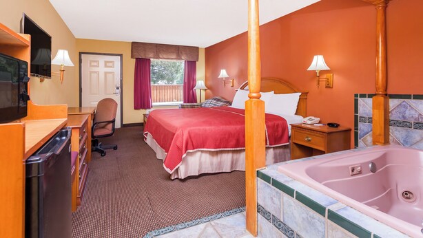 Quarto de hotel com cama, escrivaninha, cadeira, televisão, banheiro com banheira e janela com cortinas.