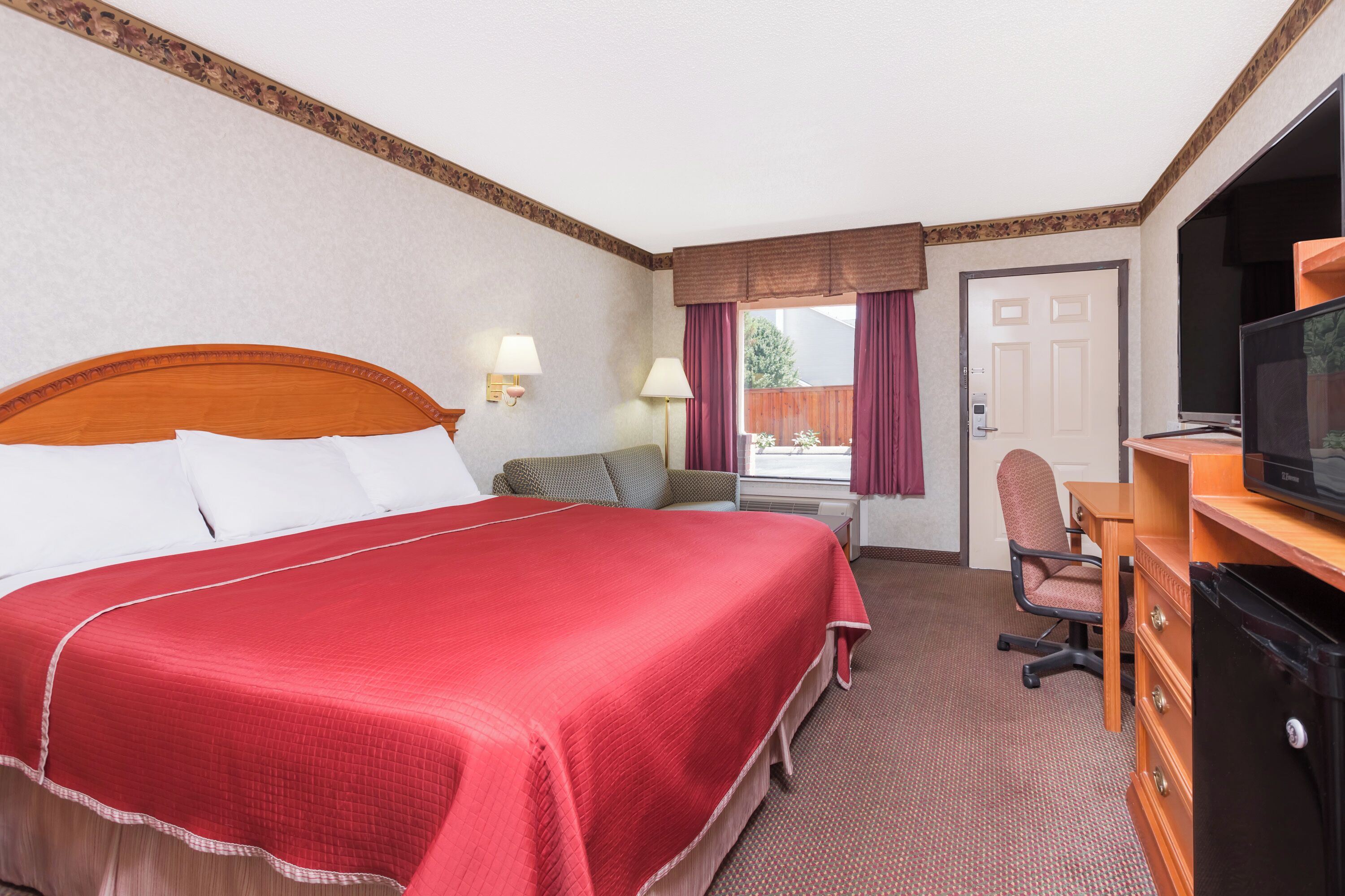 A hotel room with a large bed, a desk with a television, a chair, and a window with curtains.