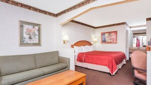 Quarto de hotel com sofá, cama com colcha vermelha, mesa de madeira e duas luminárias fixadas na parede.