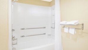 Uma banheira branca com cortina de chuveiro, um porta-toalhas com toalhas e uma porta com barra para toalhas.