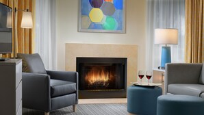 A modern living room with a fireplace, two armchairs, a coffee table, and a side table with wine glasses.