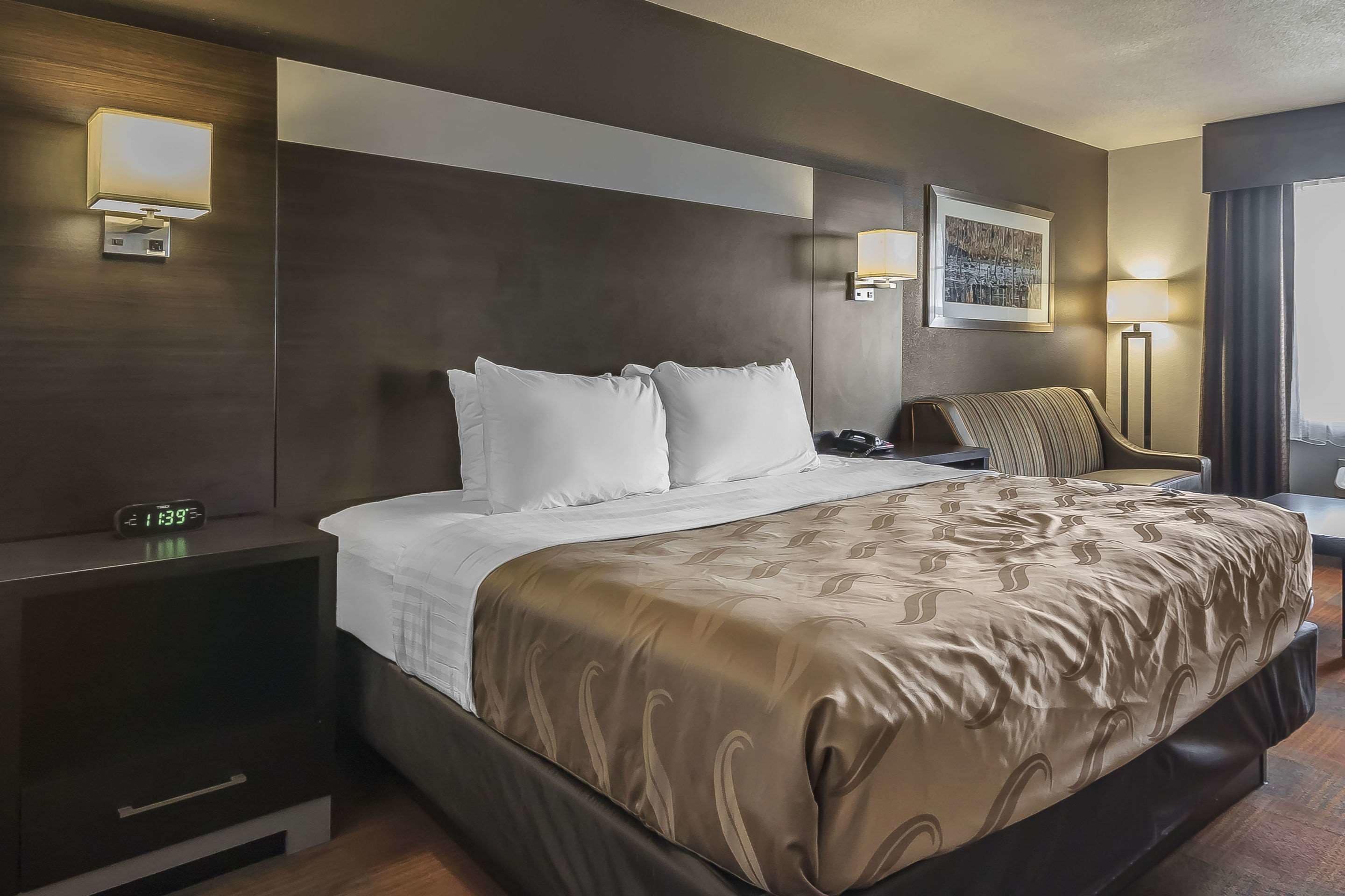 Habitación de hotel con una cama grande, mesitas de noche, un escritorio con una silla y una ventana con cortinas.