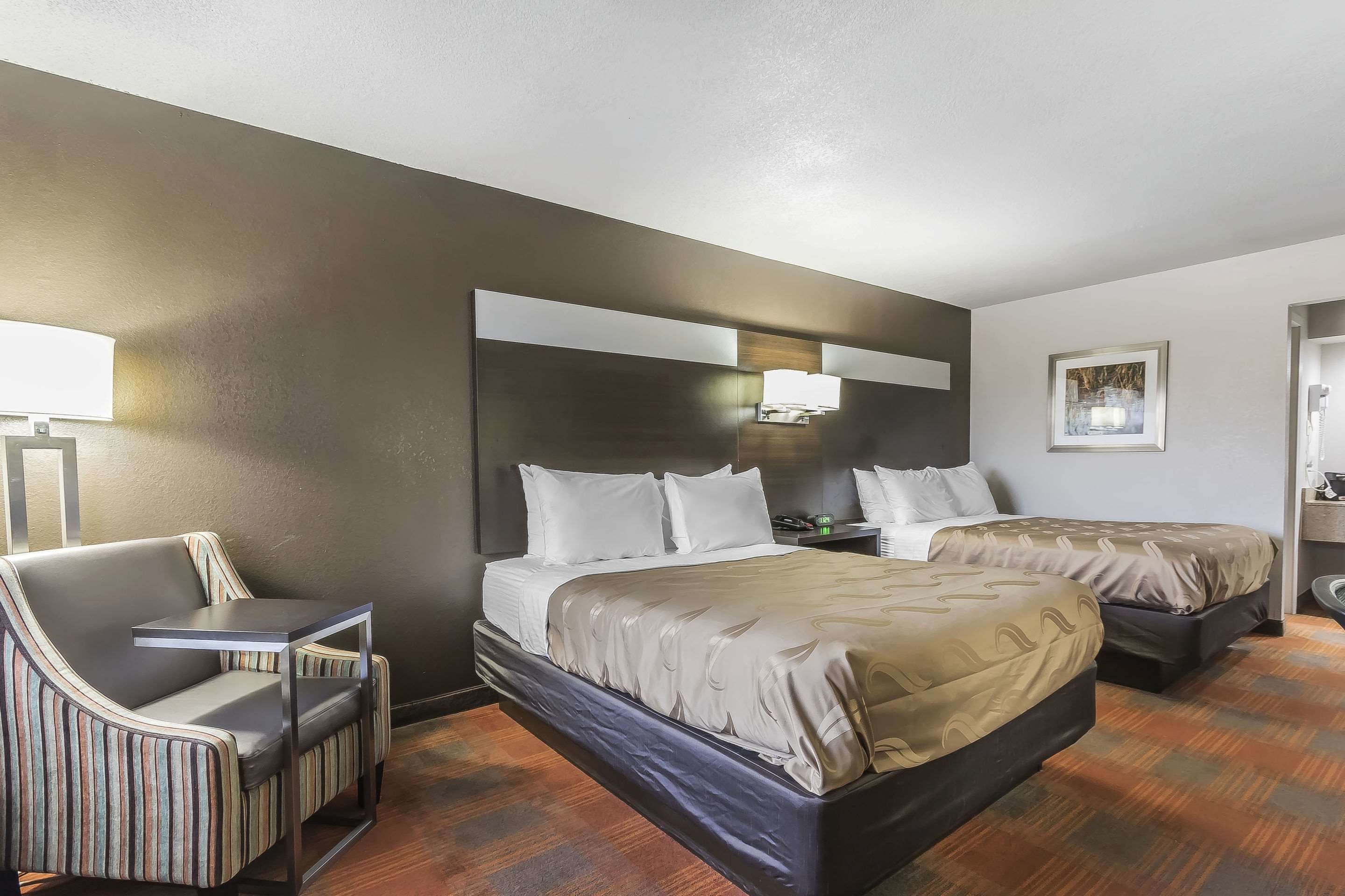 Una habitación de hotel con dos camas, un sofá, una mesita y una lámpara de noche.