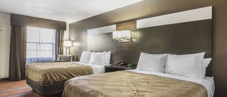 Habitación de hotel con dos camas, un ventanal grande con cortinas, una mesita de noche con lámpara y una lámpara de pared.