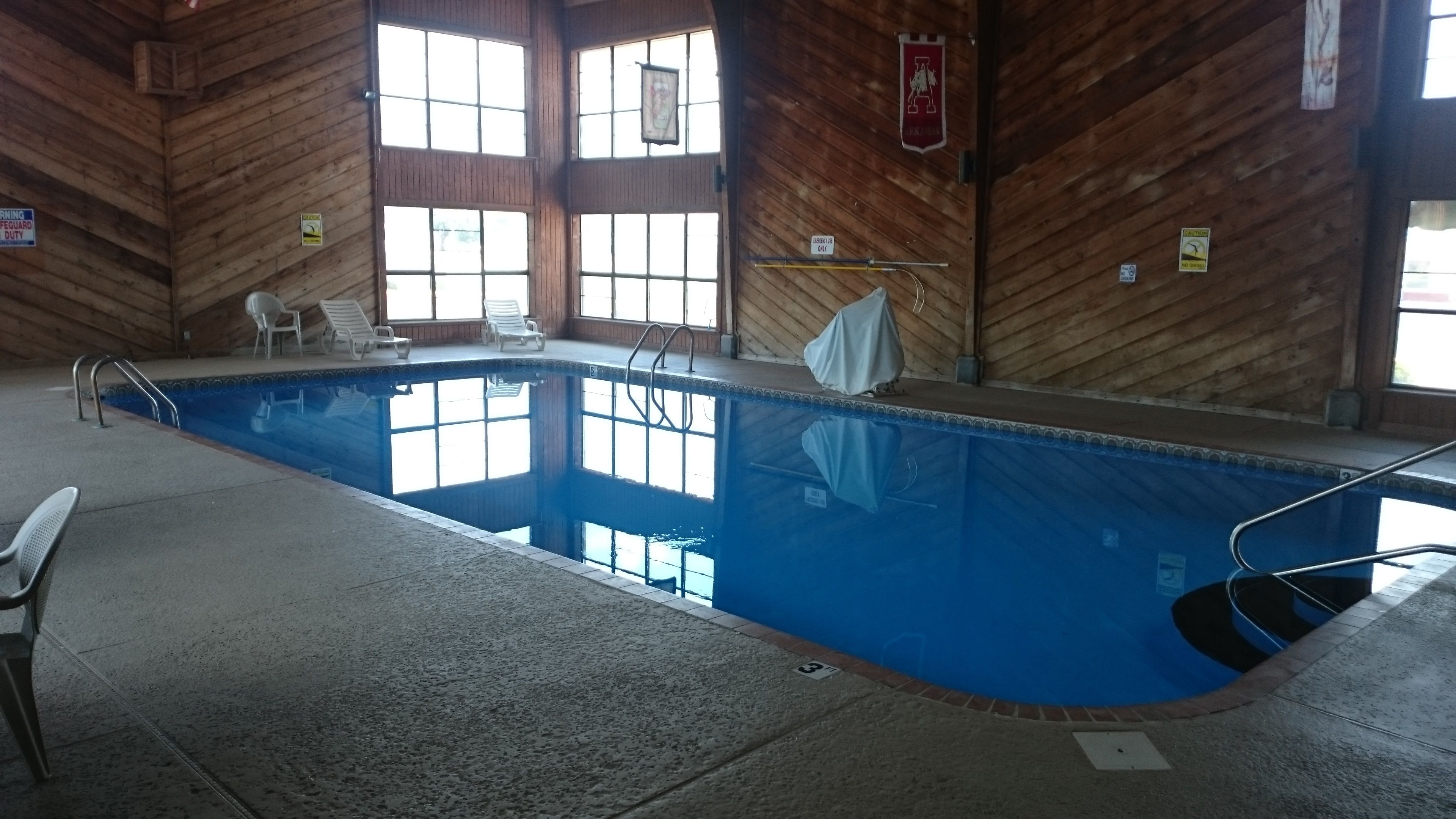 Uma piscina interior com água cristalina, rodeada por paredes de madeira e grandes janelas.